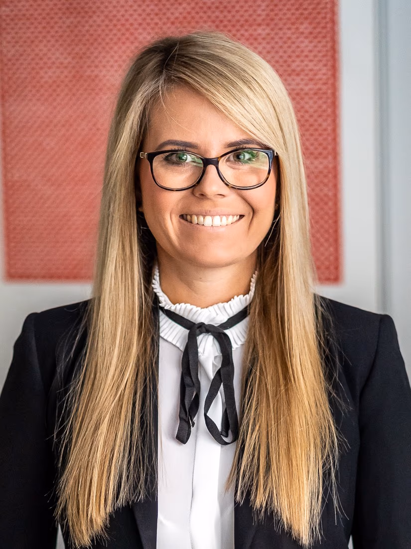 Adwokat Marlena Wiktor-Popławska w swojej kancelarii — uśmiechnięta, w czarnym garniturze, na tle koralowej grafiki